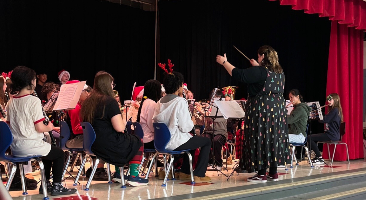 Woman conducts a group of students playing in a band on a stage